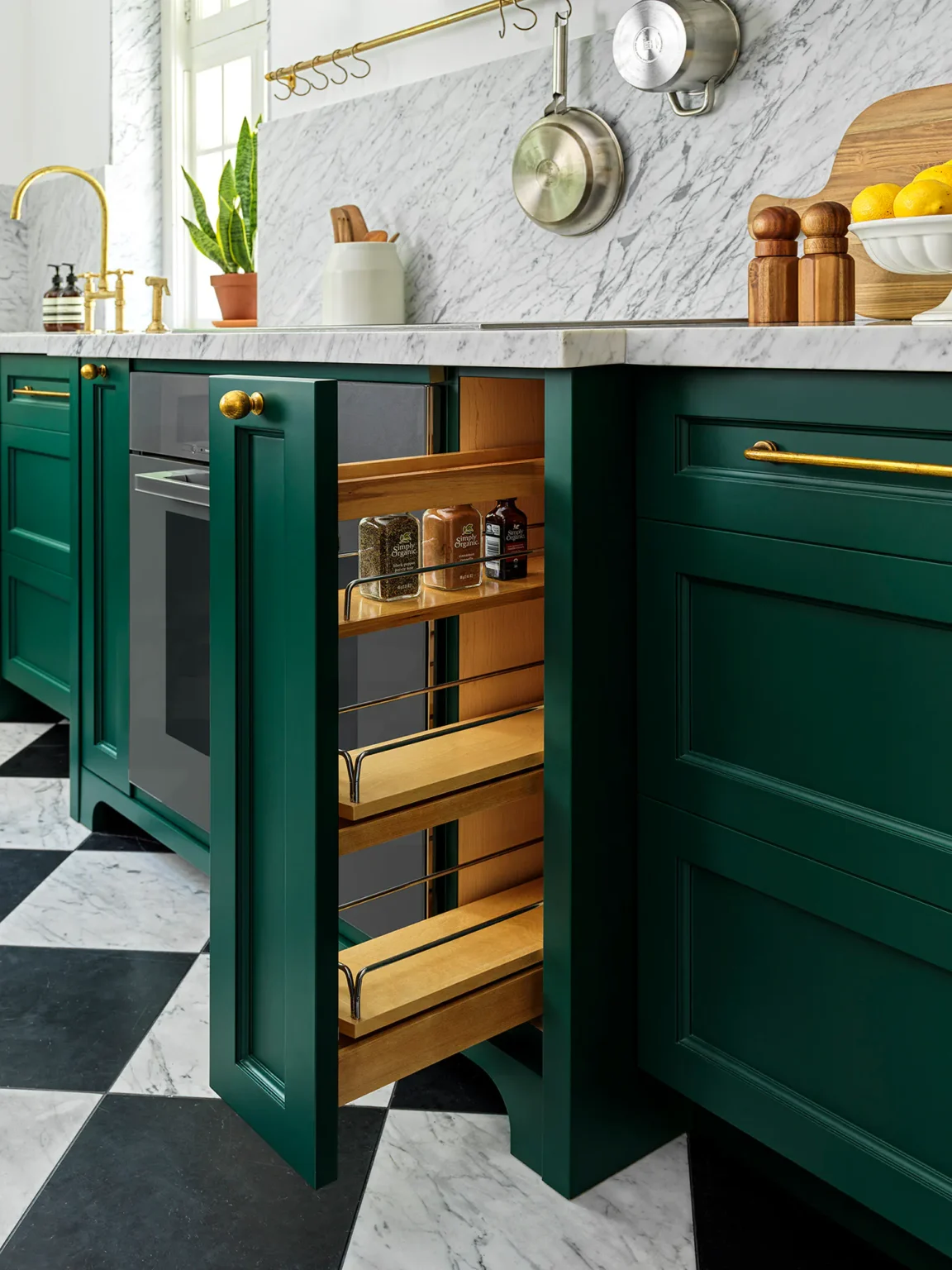 Narrow pull-out storage in green cabinetry below a marble countertop