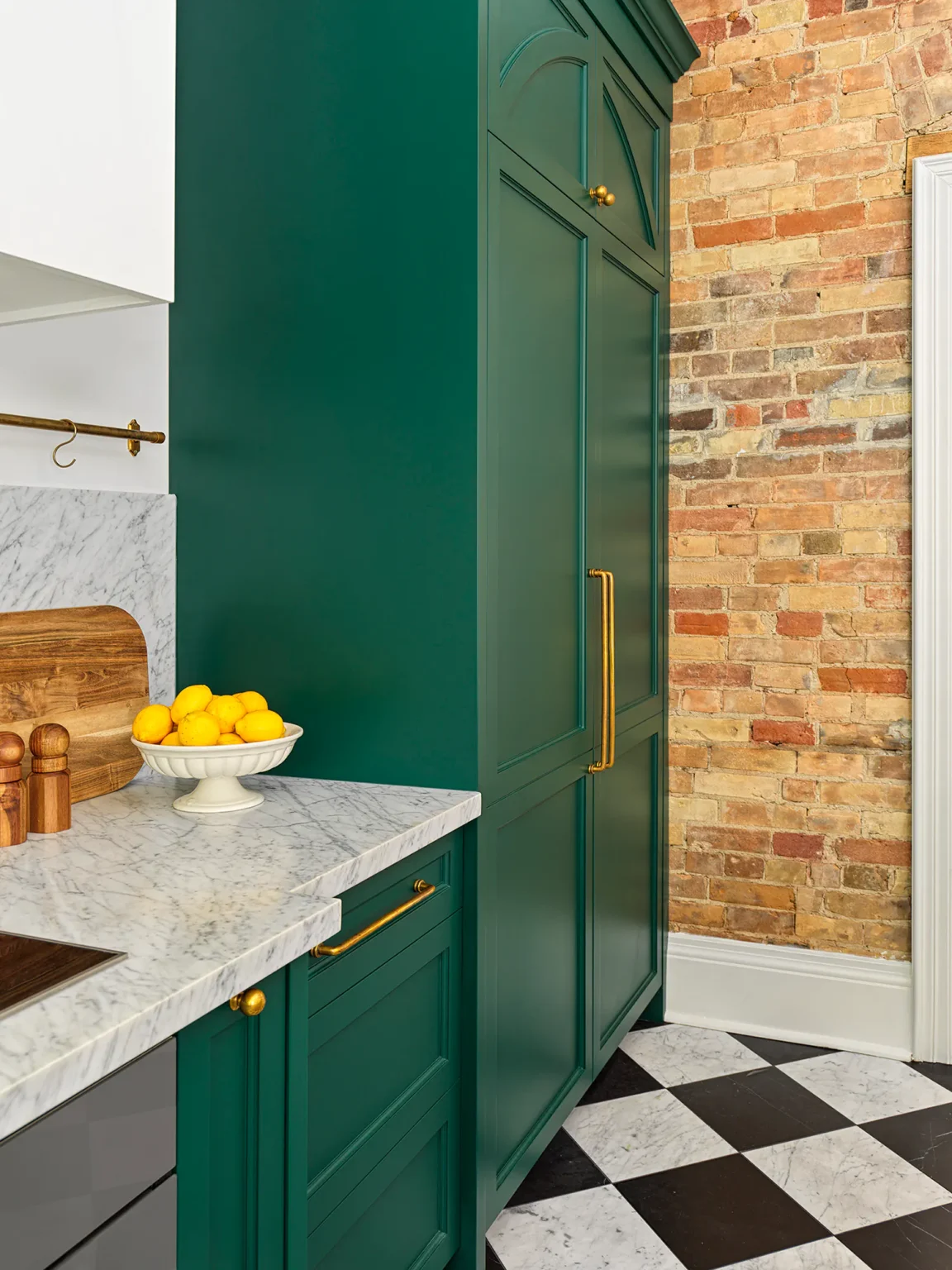 Furniture-style refrigerator cabinetry beside an exposed brick wall