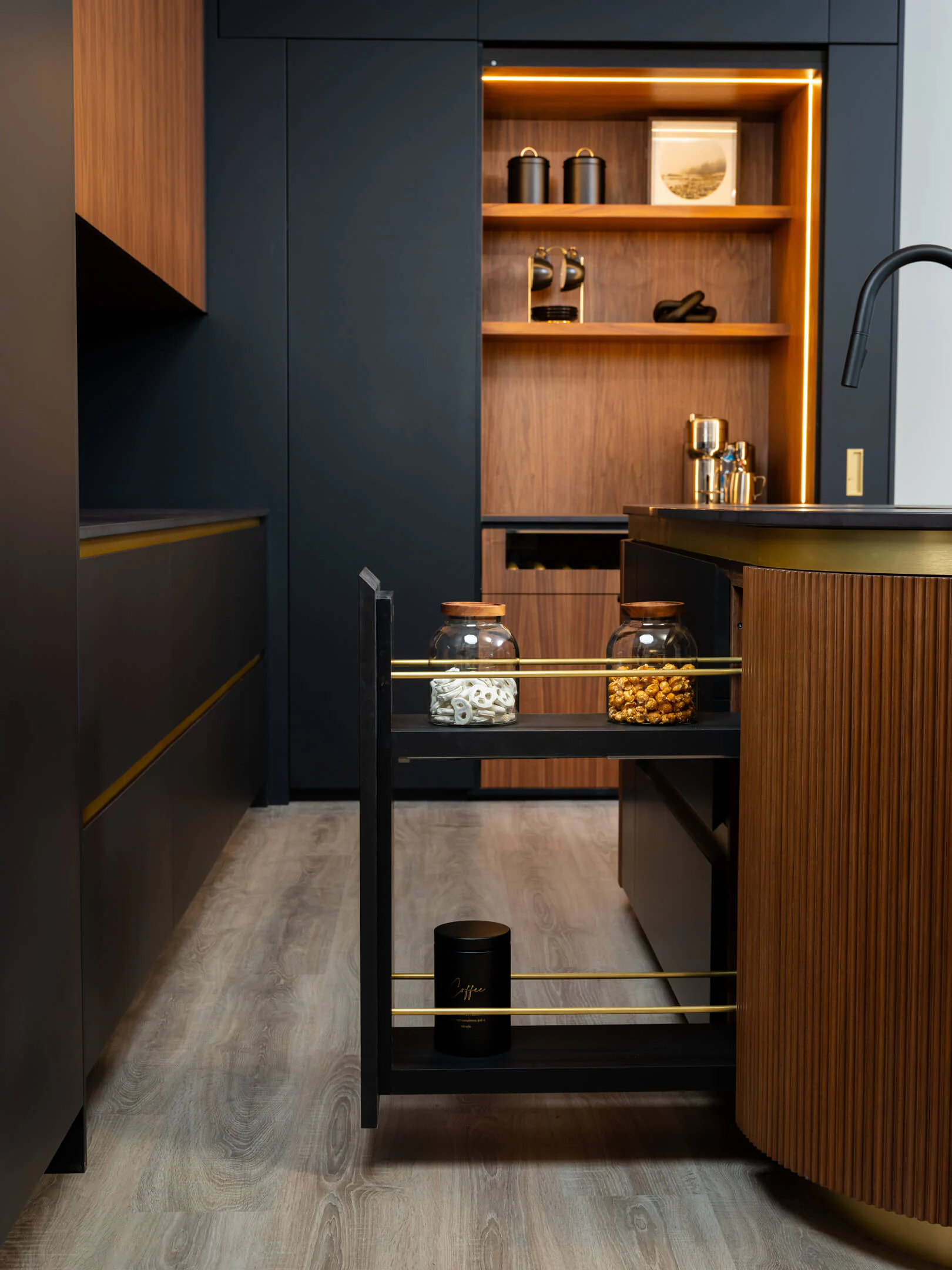 Curved reeded walnut island beside matte-black cabinetry and an open pull-out