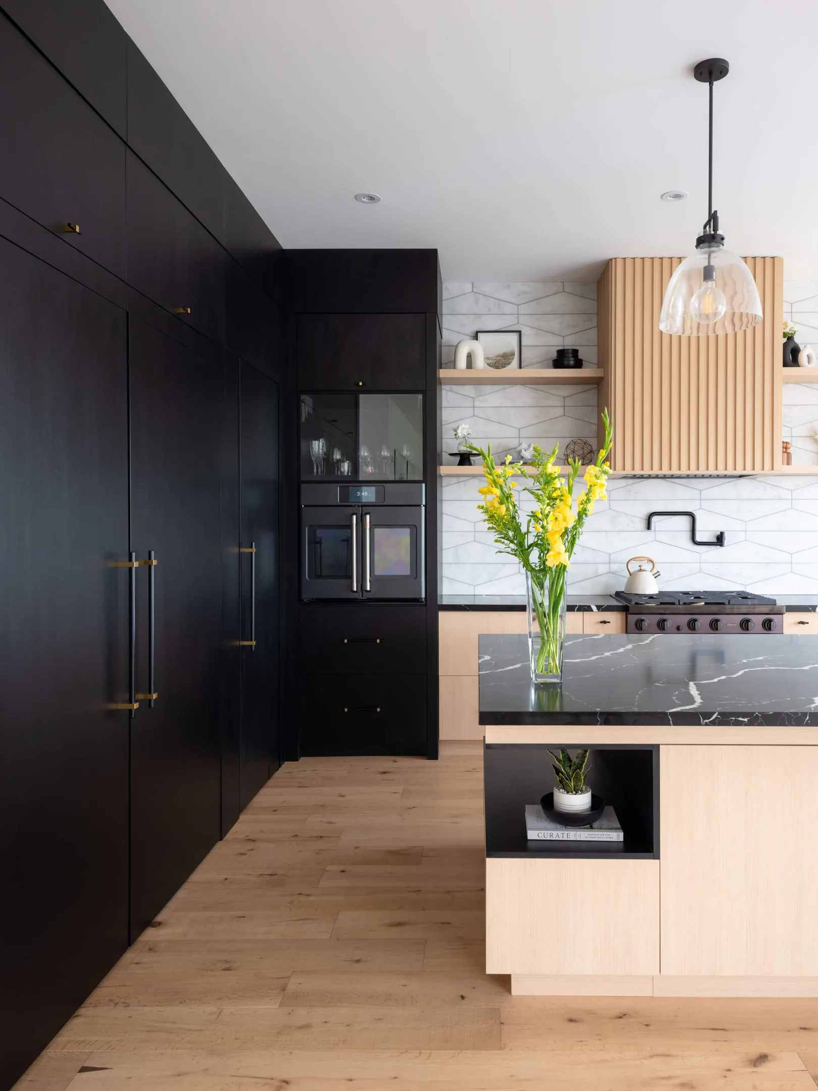 Dark cabinetry wall beside a light wood island with a black stone top