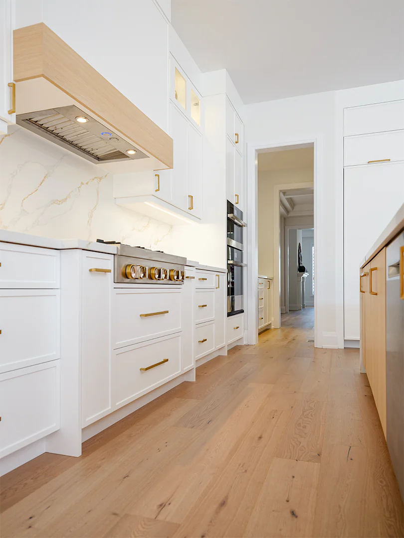 Range wall with a white oak hood accent beside painted tall cabinetry