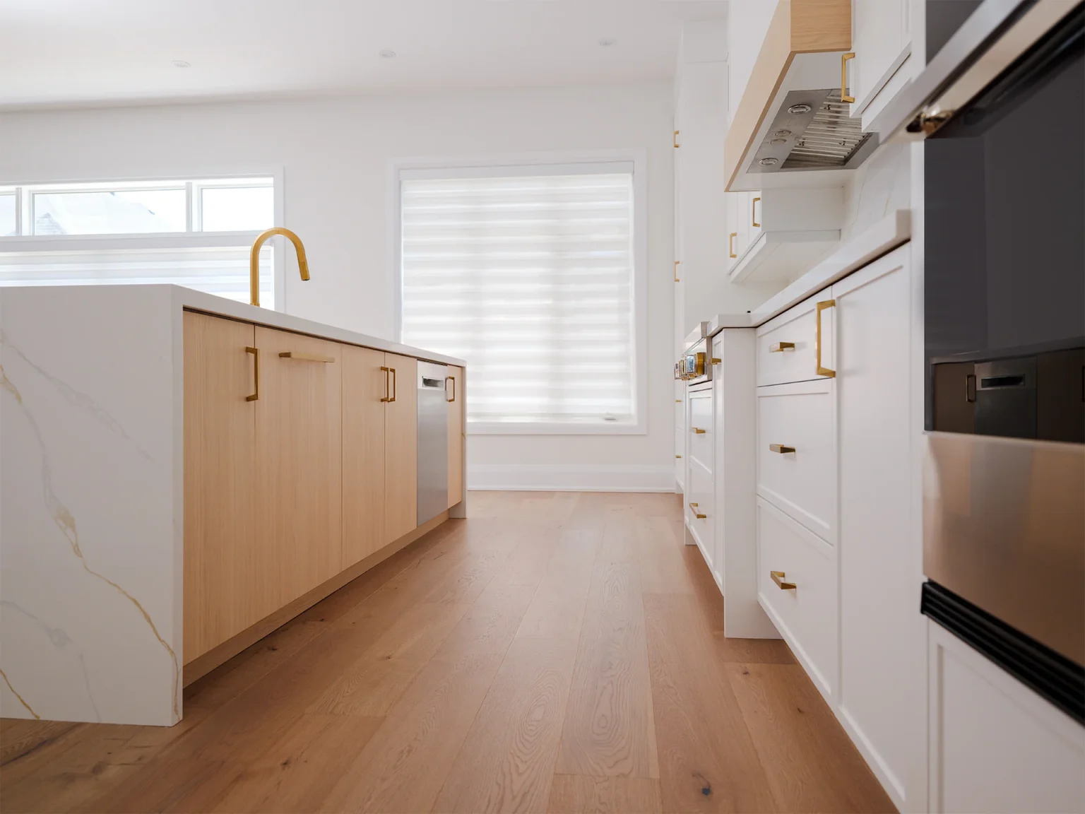 Painted perimeter cabinetry and the white oak island seen down the length of the kitchen