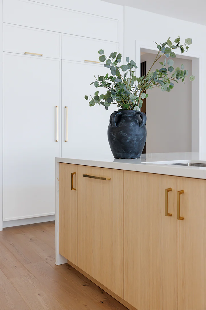 White oak island with brass pulls beside painted panelled cabinetry