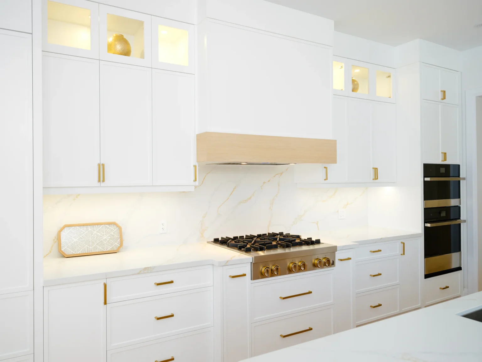 Range wall with illuminated glass-front cabinets and a white oak hood accent