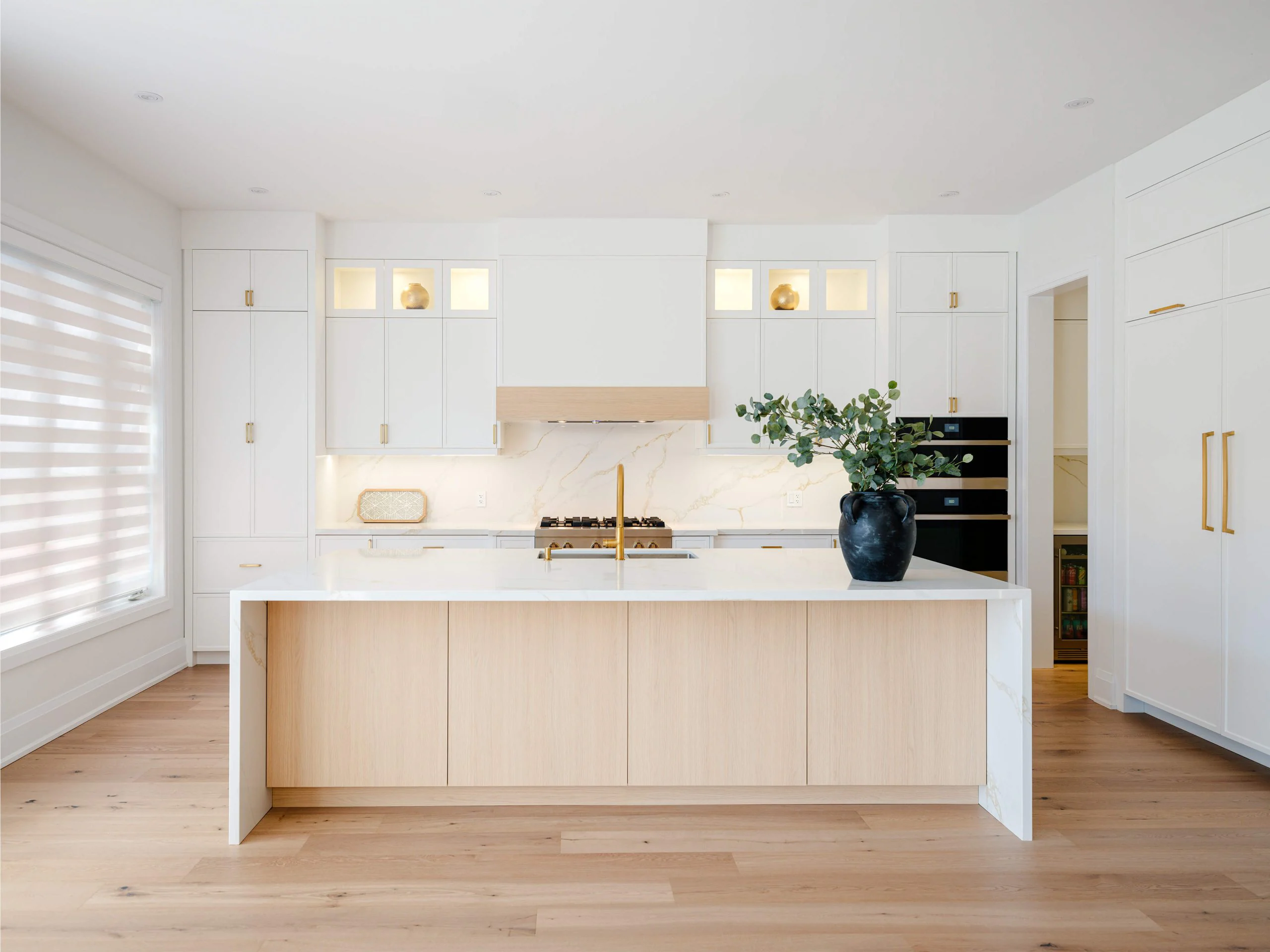 Bright kitchen with painted cabinetry and a white oak island within a stone waterfall surround