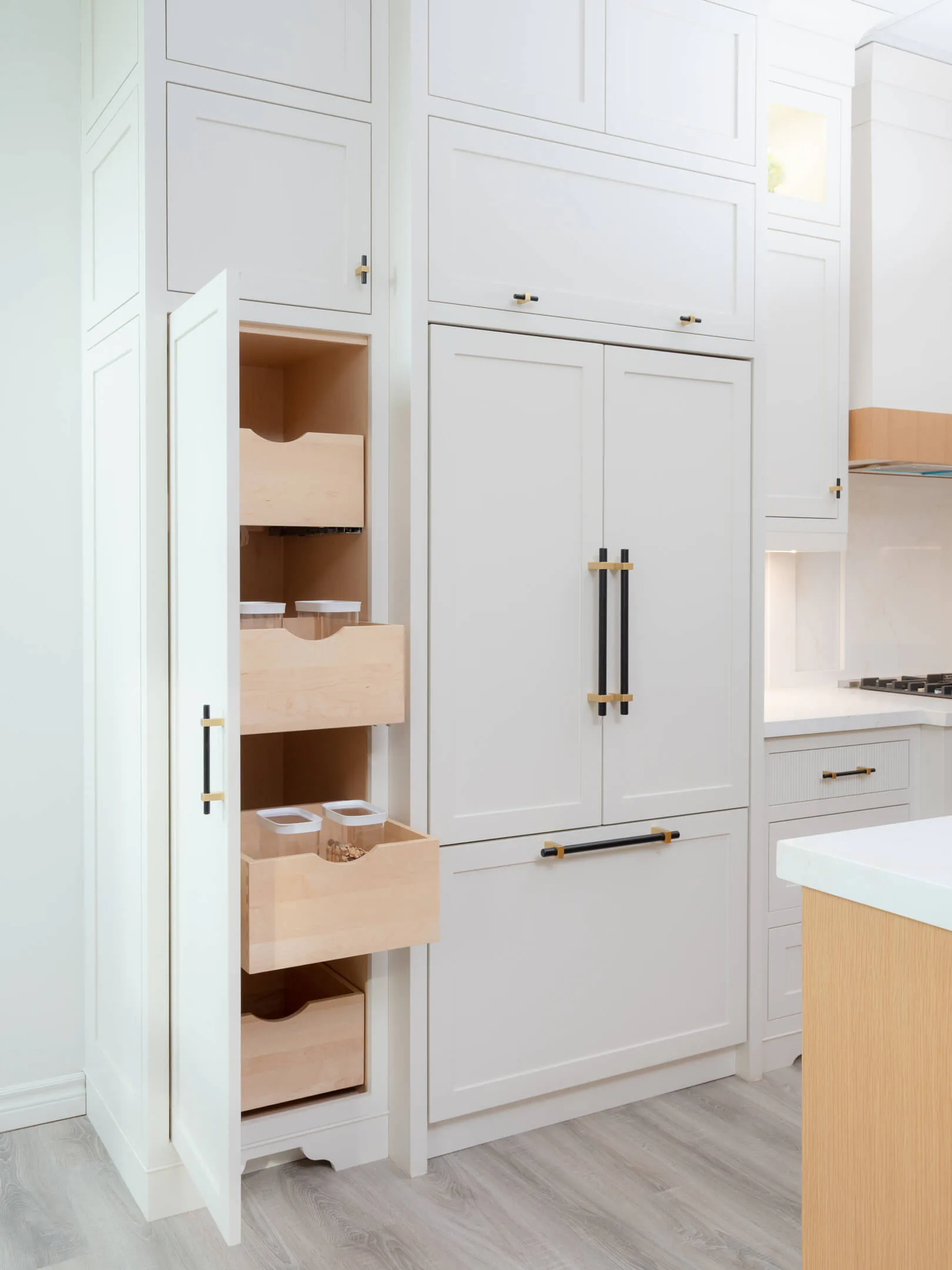 Pull-out pantry drawers with white oak interiors beside panelled cabinetry