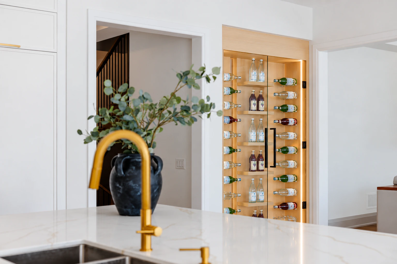 Illuminated white oak display cabinet with glass doors, seen from the kitchen island